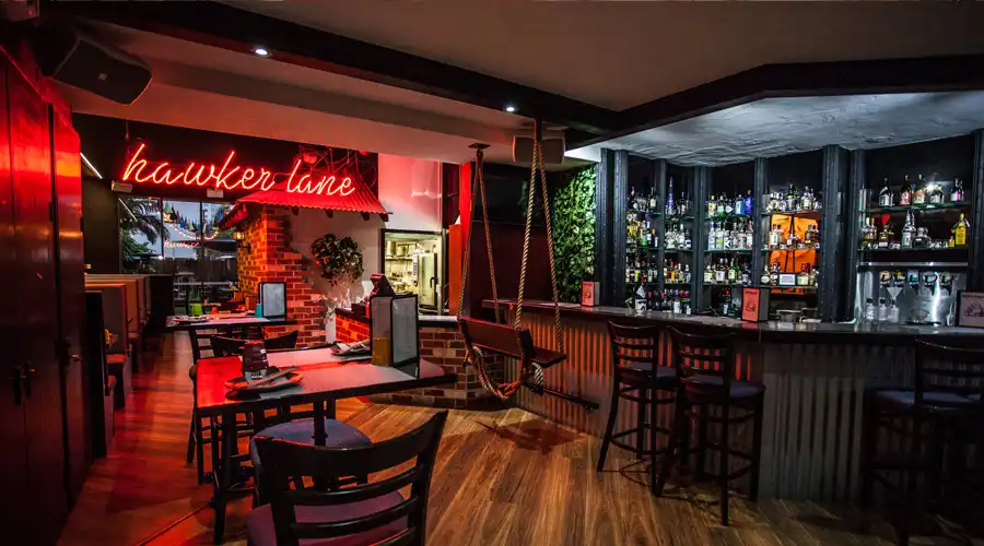 Restaurant interior with bar, swing seat, and "hawker lane" neon sign.