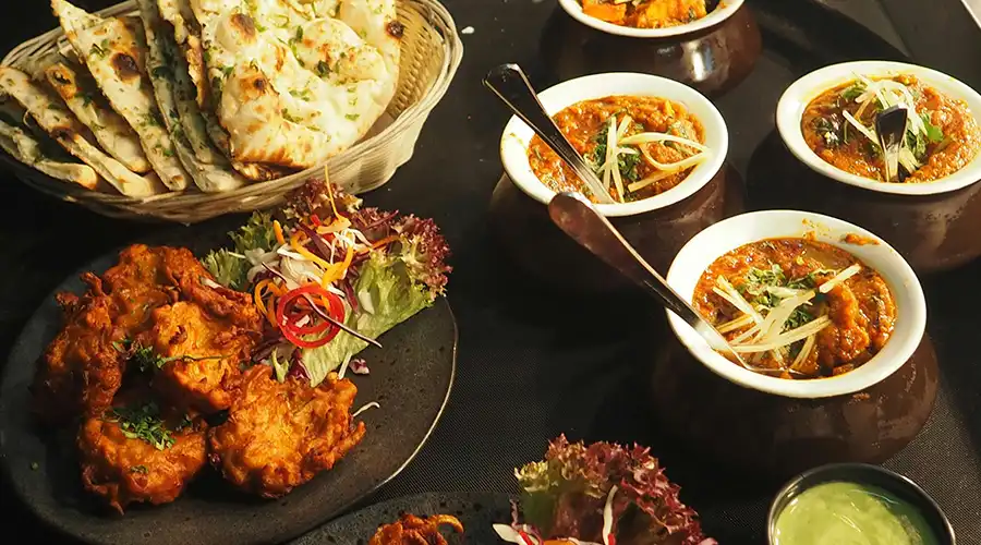Flatlay of bright indian dishes and naan with spoons in some of the curries