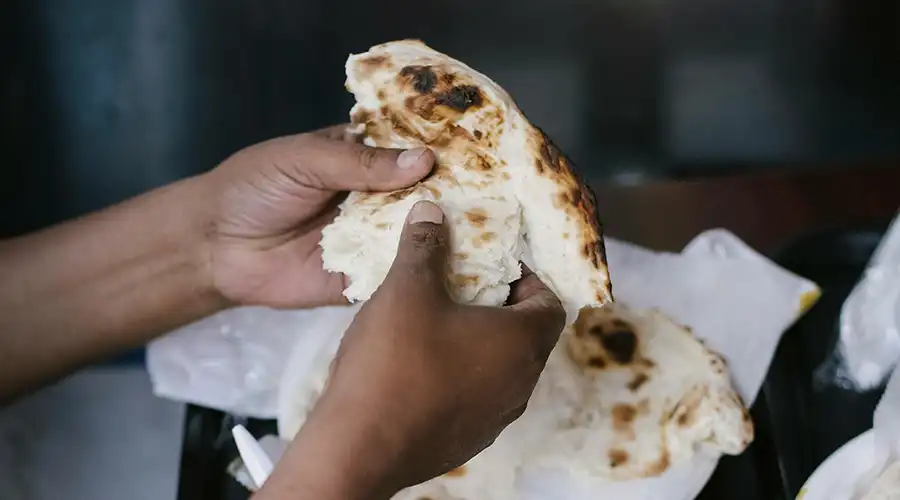Hands tearing fresh naan bread