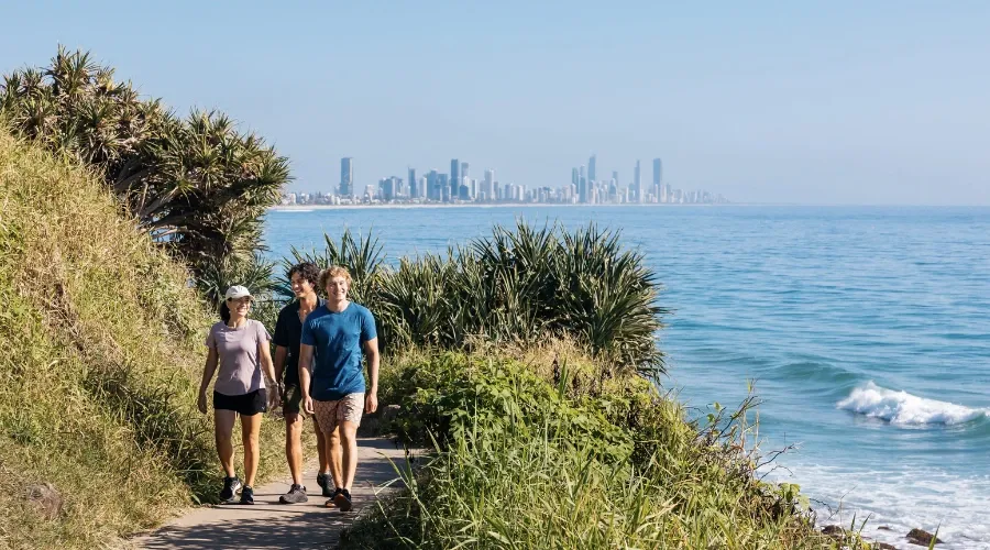 A group of friends walk along a walking track with Gold Coast in the backdrop