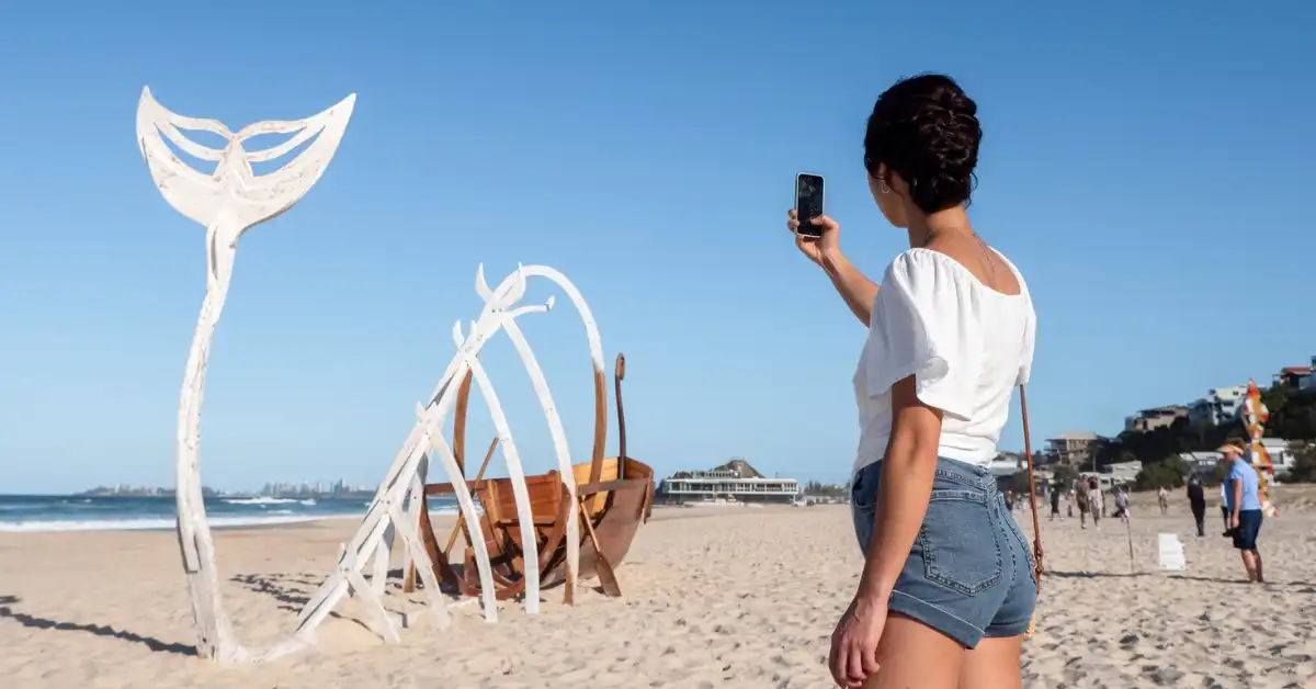 A woman photographs a sculpture on Currumbin Beach at SWELL Festival