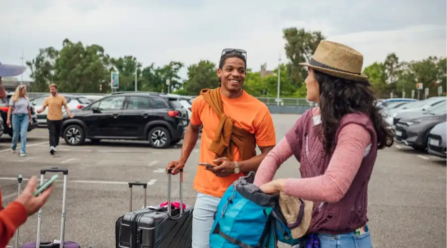 Two travellers with luggage in a car rental car park