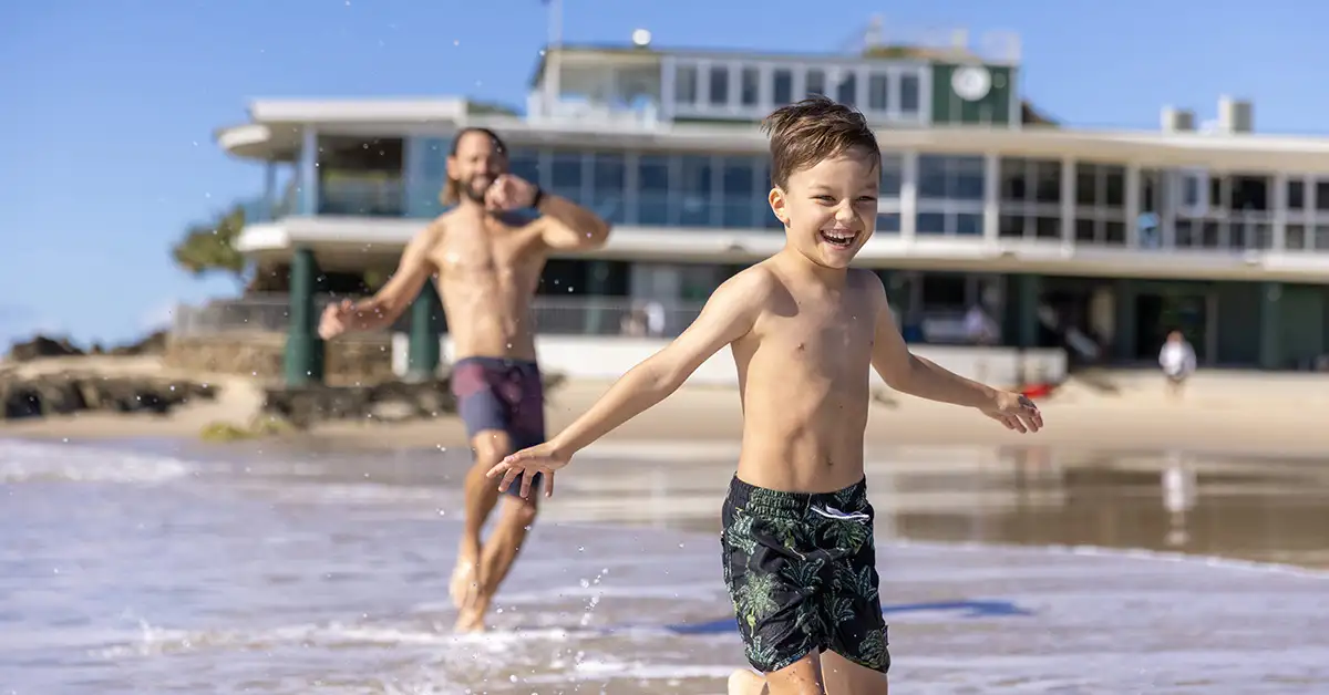 father and son splash in the waves at currumbin beach vikings surf club