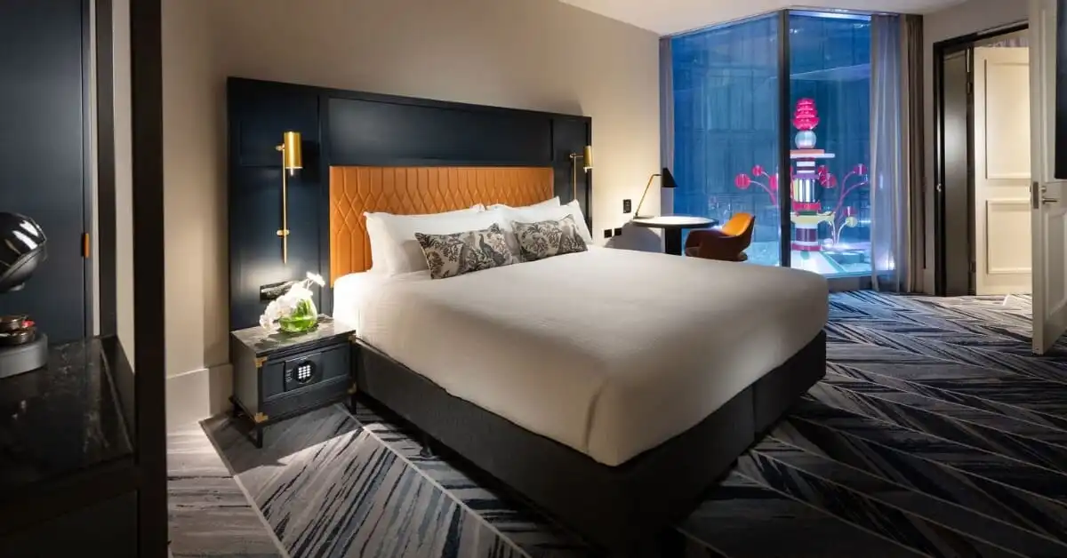 A stylish hotel room with a modern design features a large bed, a sleek workspace, and a vibrant window display at Dorsett Melbourne