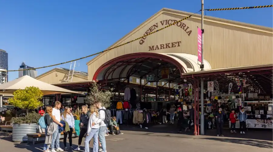 Visitors strolling out the front of Queen Victoria Market in Melbourne, enjoying a lively atmosphere with various stalls which represents a vibrant cultural hub.