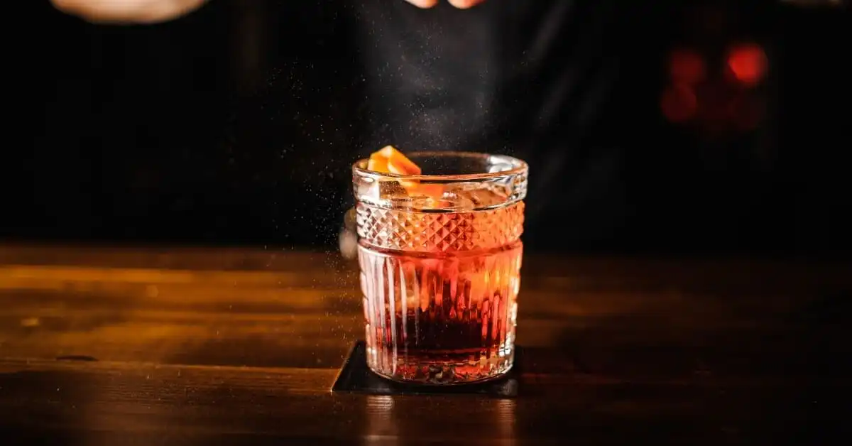 A vibrant berry cocktail in a textured glass, garnished with a twist of orange, ready to be savoured.