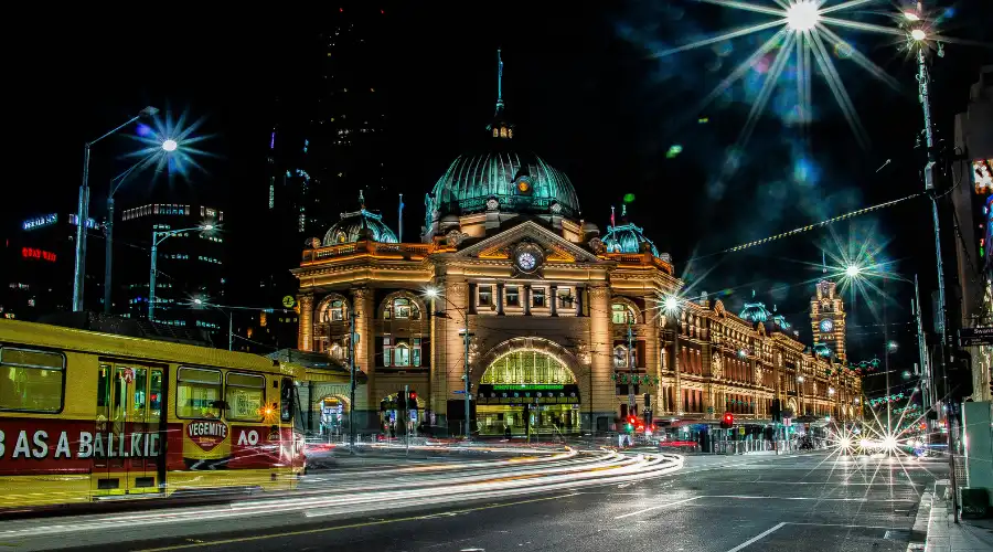 Flinders Street Station at night in Melbourne CBD with tram and city lights.