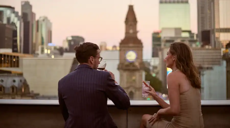 A couple sip on a rooftop bar overlooking Melbourne’s CBD