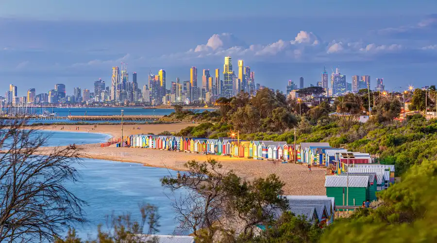 Brighton Beach colorful bathing boxes with Melbourne city skyline at dusk
