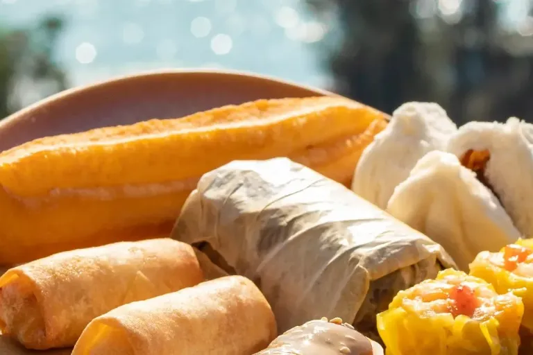 A platter featuring popular Chinese dim sum and breakfast foods like fried dough sticks, wrapped sticky rice and steamed pork buns.