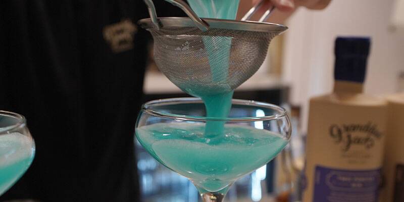 Blue cocktail being poured in martini glass